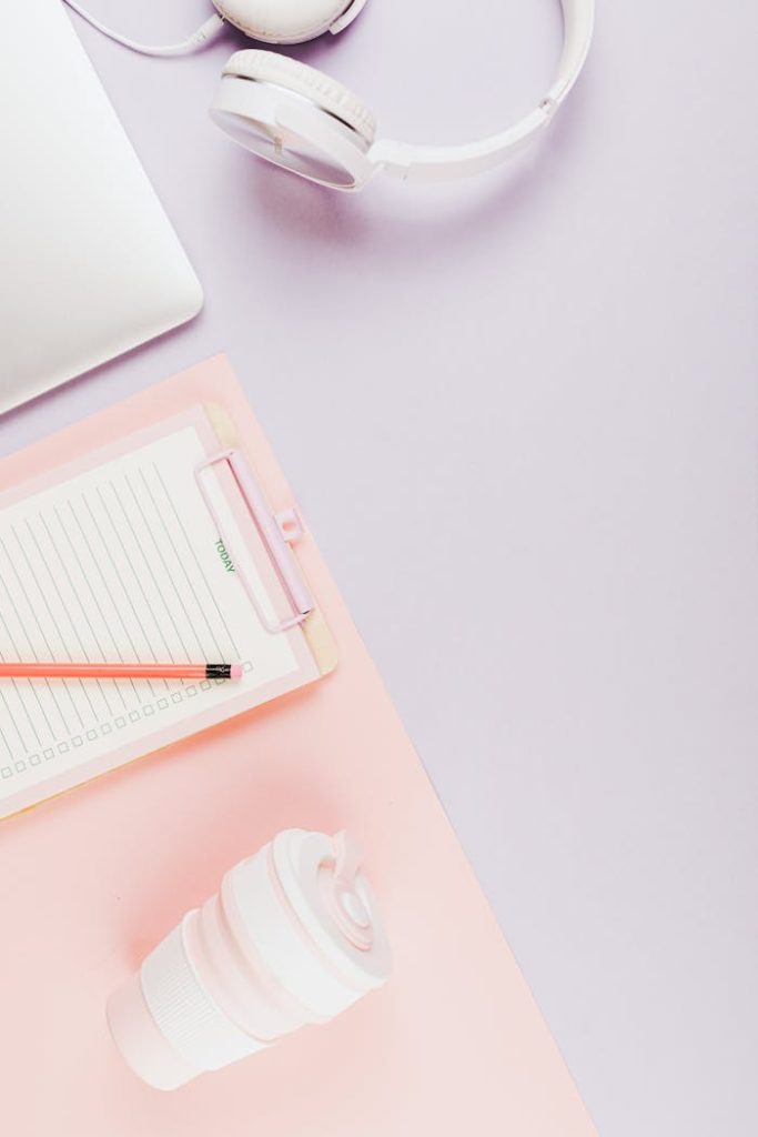 Overhead view of a pastel-toned workspace with headphones, notebook, and coffee cup.